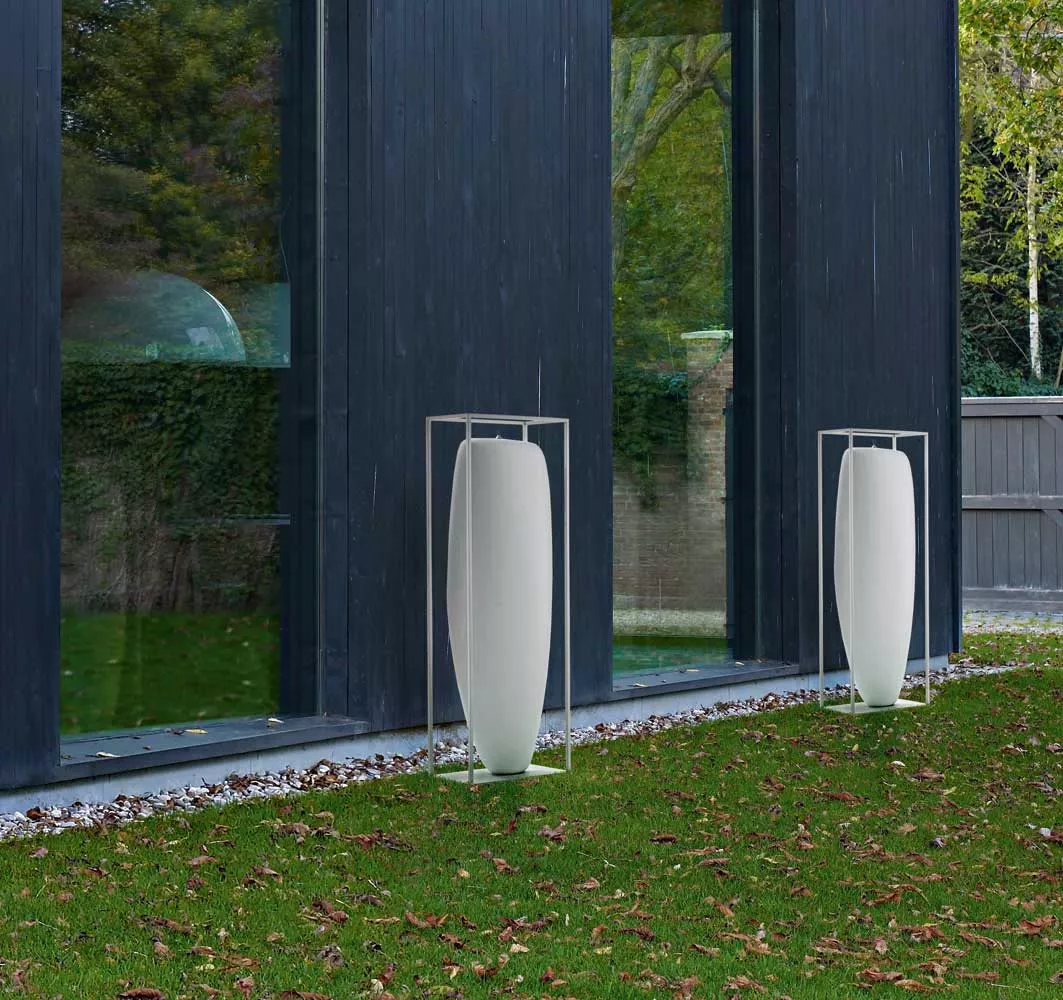 Zwei B&B Italia Overscale Flames Outdoor Kerzen stehen vor einem modernen Gebäude mit großen Fenstern und einem Garten im Hintergrund.