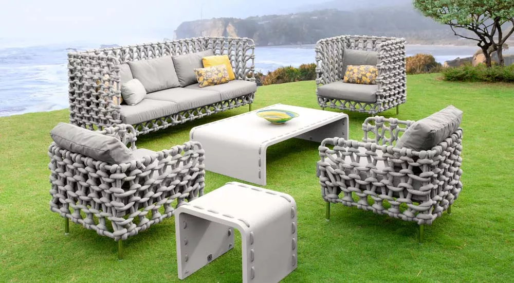 Gartenmöbel-Set von Kenneth Cobonpue, Modell Cabaret, in Grau auf einer Wiese mit Meerblick, bestehend aus Sofa, Sesseln und Tisch.