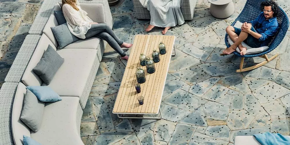 Drei Personen entspannen auf Dedon Lou Kollektion Gartenmöbeln auf einer Terrasse mit Steinboden und einem Holztisch in der Mitte