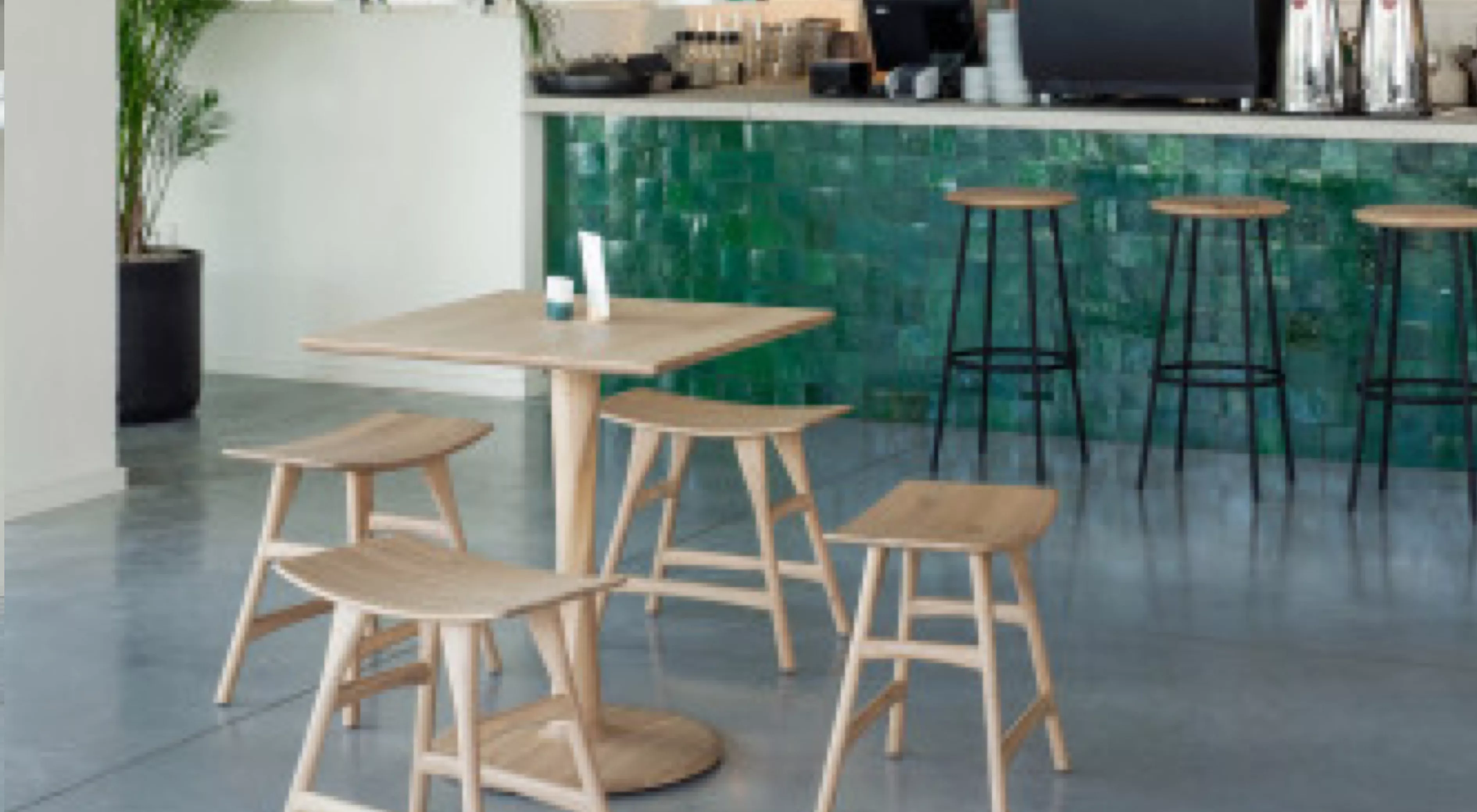 Holzstühle und -tisch von Villa Schmidt in hellem Holzton vor einer Bar mit grüner Kachelwand auf grauem Betonboden in modernem Café.