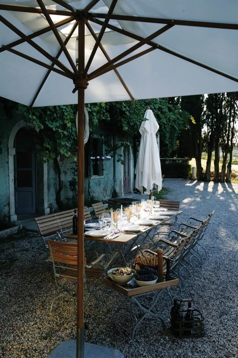 Weißer Teakschirm von Weishäupl, quadratisch, 250 x 250 cm, über einem gedeckten Tisch im Garten mit Kiesboden und Bäumen im Hintergrund.