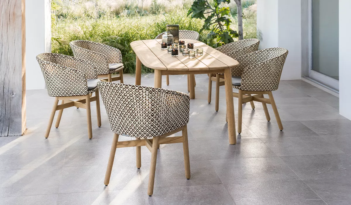 Gartenstühle mit Teakholzgestell und Kunststoffgeflecht auf Betonoptik-Fliesen und Teakolz-Tisch.