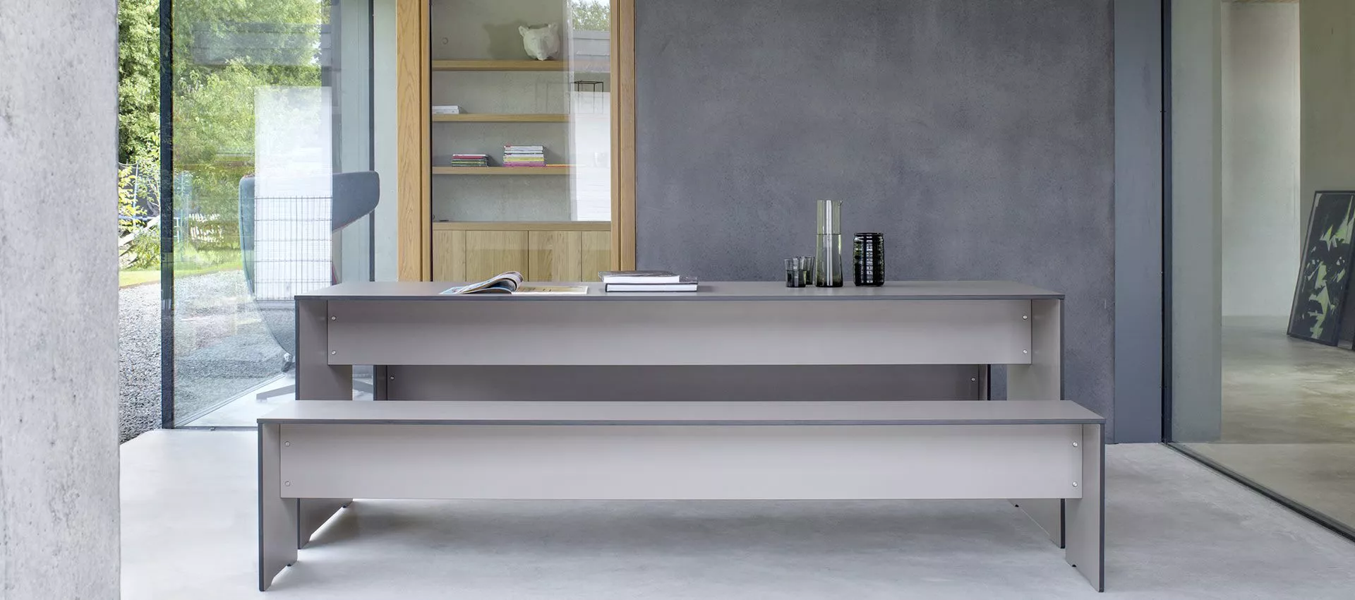 Conmoto Riva Gartentisch Essgruppe in Grau, moderne Essgruppe in minimalistischem Design, auf Betonboden vor einer Glaswand.