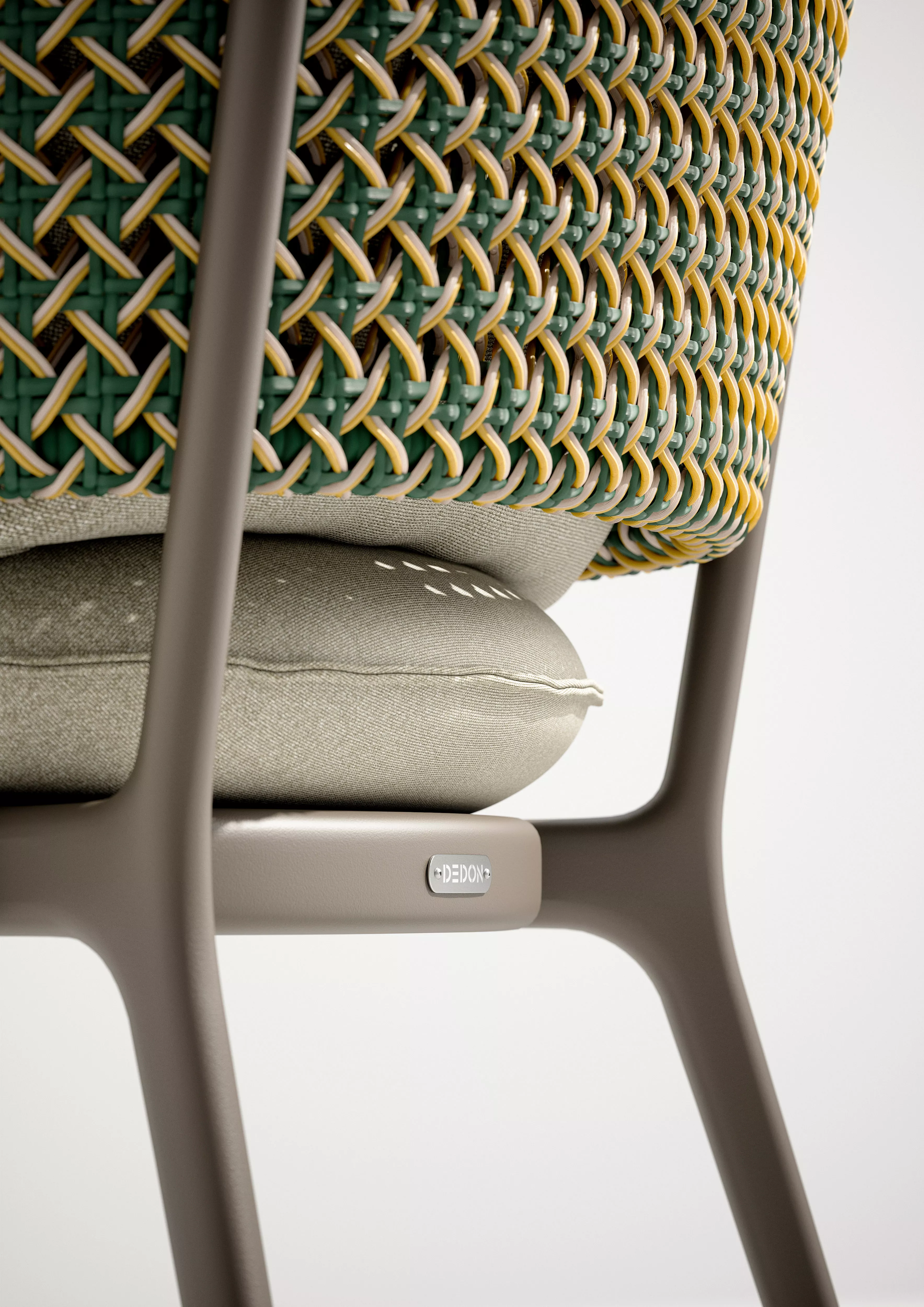 Nahaufnahme des DEDON BELLMONDE Stuhls mit grün-gelbem Geflecht und beigem Kissen ohne Hintergrund