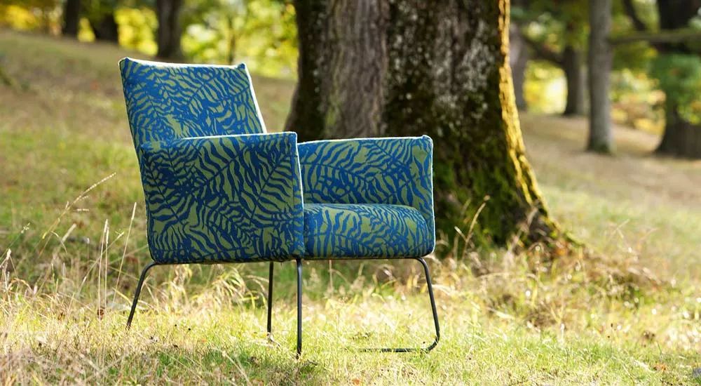 Fischer Möbel Kalos Loungesessel in Blau-Grün auf einer Wiese vor einem Baum, stimmungsvolles Outdoor-Bild.