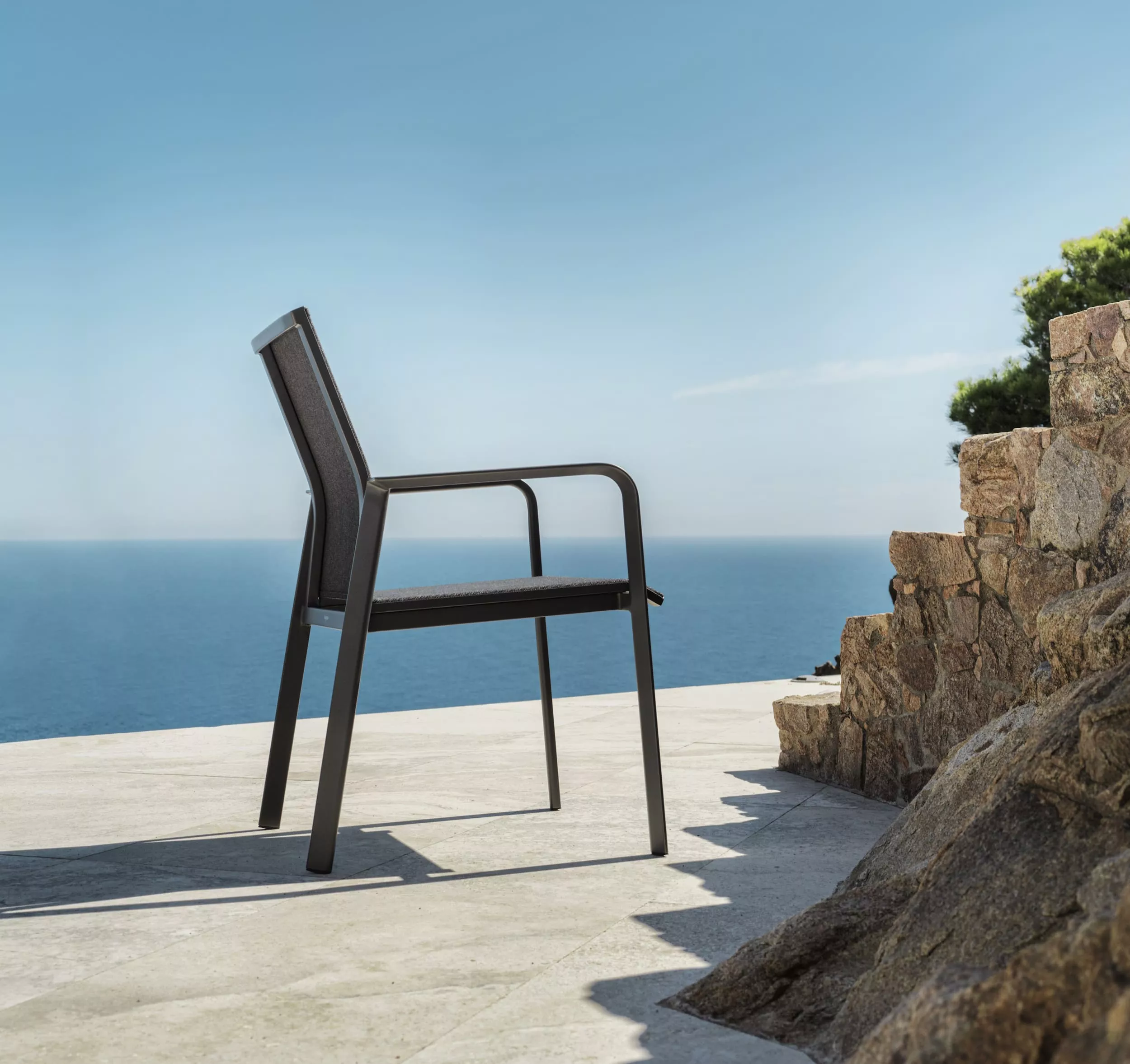 Solpuri Breeze Stuhl steht auf einer Terrasse mit Meerblick und Steinmauer im Hintergrund Mood Bild