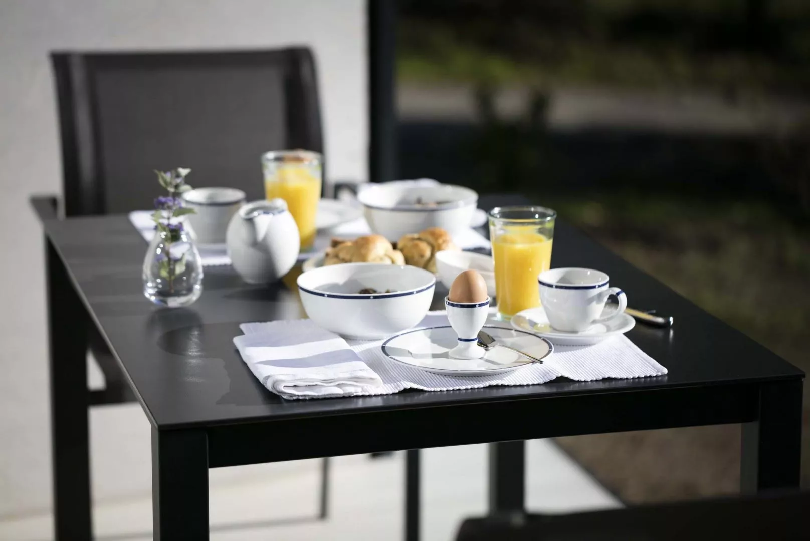 Todus Puro Esstisch in Schwarz, gedeckt mit Frühstücksgeschirr und Orangensaft, auf einer Terrasse bei Tageslicht.