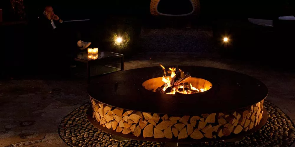 Ein Mann sitzt bei Kerzenschein und genießt die Atmosphäre während ein Ak-47 Feuerstellen Zero Feuerstelle im Freien brennt.