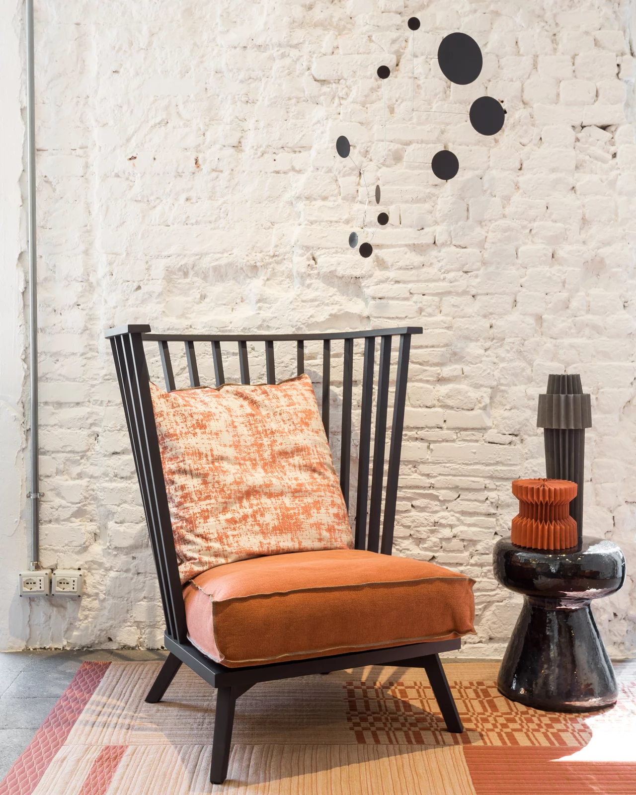 Ein Gervasoni Sessel mit orangefarbenem Kissen steht vor einer weißen Backsteinwand neben einem schwarzen Beistelltisch mit Dekoration