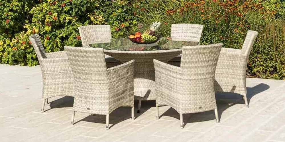 Alexander Rose Ocean Pearl Lounge in Beige auf einer Terrasse mit grünem Hintergrund, bestehend aus einem runden Tisch und sechs Stühlen.