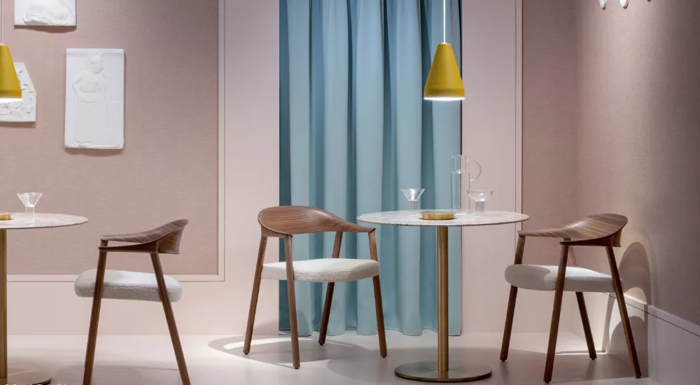 Drei Pedrali-Stühle in Holzoptik mit weißen Sitzpolstern stehen um runde Marmortische in einem modern eingerichteten Raum mit blauen Vorhängen.