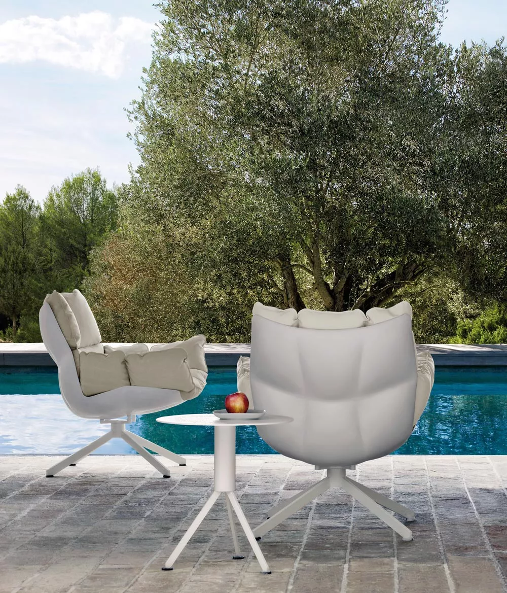 B&B Italia Husk Outdoor Loungesessel in Weiß und Beige steht neben einem kleinen Tisch mit einem Apfel im Freien vor einem Pool und Bäumen.