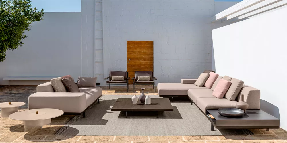 Talenti Allure Gartenmöbel-Kollektion in Beige auf einer Terrasse mit Steinboden und weißer Wand im Hintergrund, moderne Lounge-Atmosphäre.