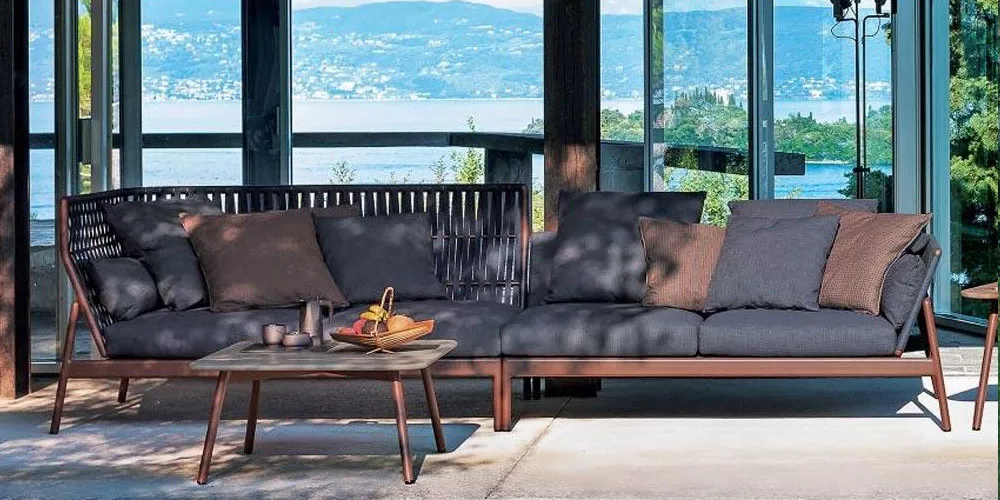 Roda Kollektion Piper Sofa in Dunkelgrau auf einer Terrasse mit Seeblick, umgeben von Glaswänden und Holzelementen.