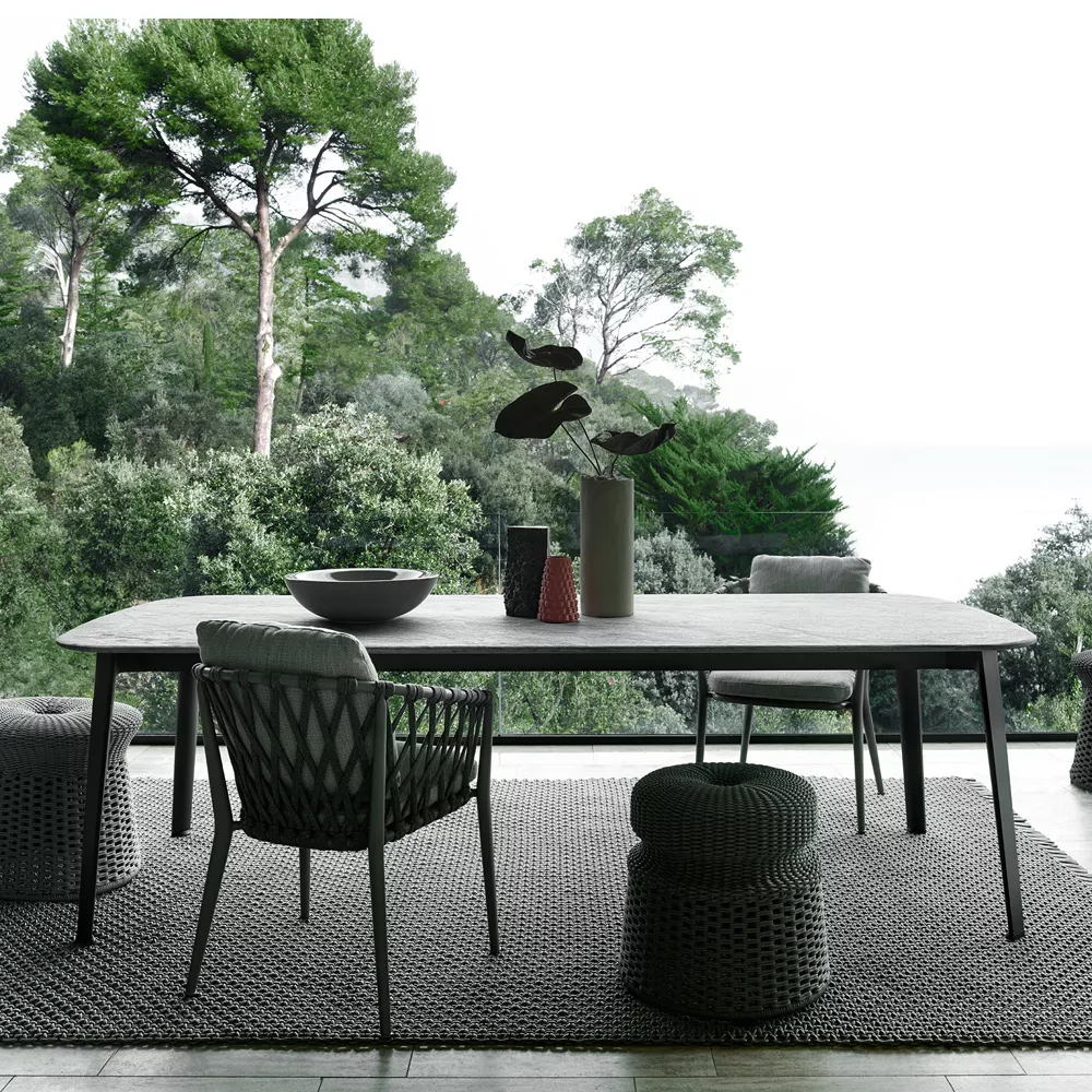 B&B Italia Ginepro Esstisch in einem modernen Außenbereich mit Blick auf einen Wald und das Meer dekoriert mit Vasen und Schalen