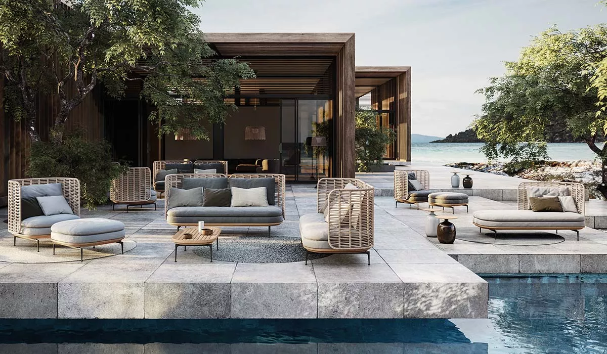 Gloster Mistral Gartenmöbel Loungegruppe in Naturtönen auf einer Terrasse mit Pool und Meerblick, umgeben von Bäumen.