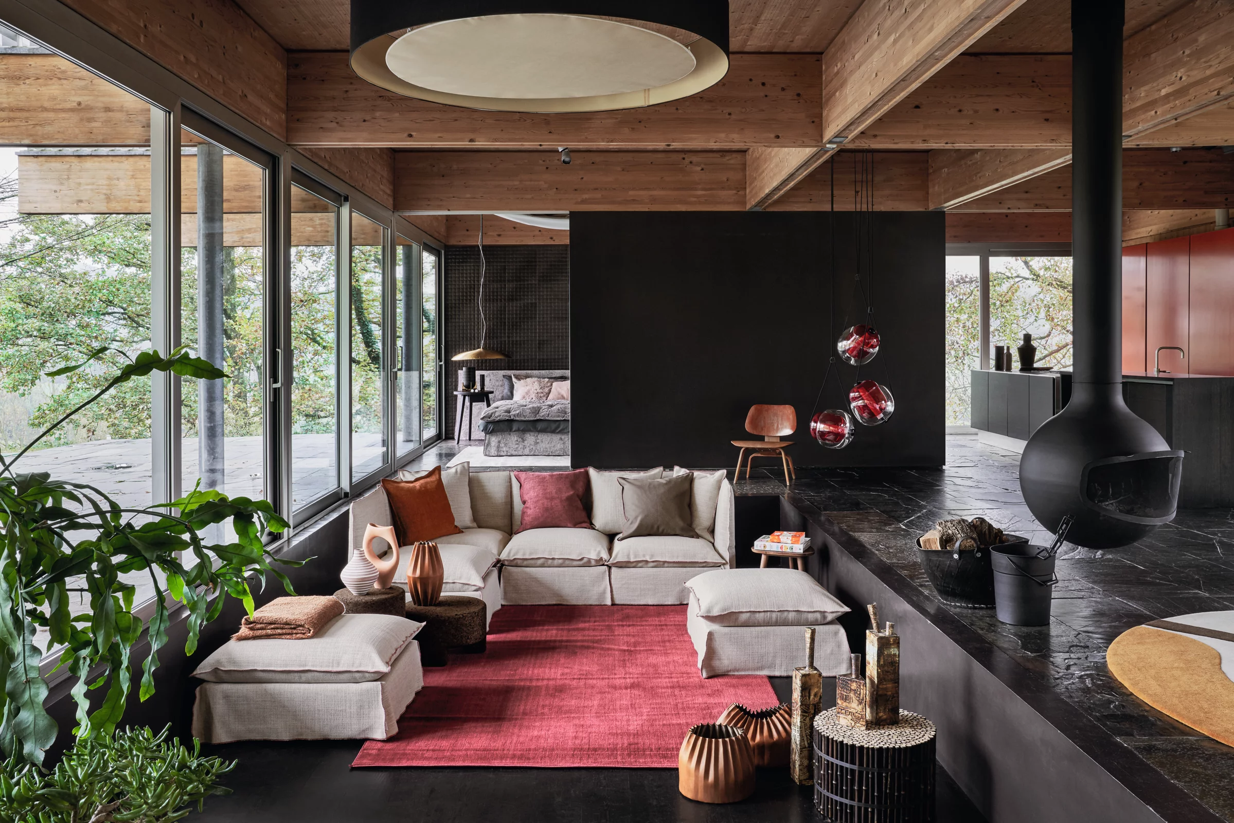 Gemütliches Wohnzimmer mit Ghost-Sofa von Gervasoni in Beige, umgeben von Holzwänden und großen Fenstern, mit rotem Teppich und Pflanzen.