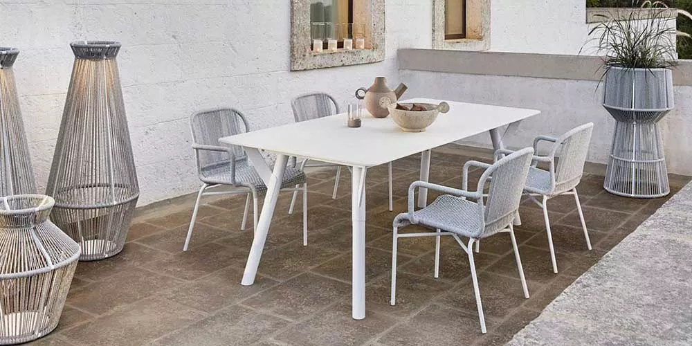 Varaschin Link Essgruppe in Weiß auf einer Terrasse mit Steinboden, bestehend aus einem Tisch und vier Stühlen, umgeben von Dekoration.