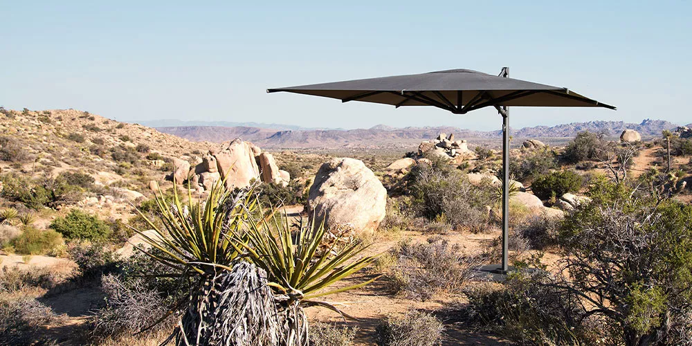 Dedon Sonnenschirm aus der Kollektion Reav in Anthrazit, aufgestellt in einer felsigen Wüstenlandschaft unter klarem Himmel.