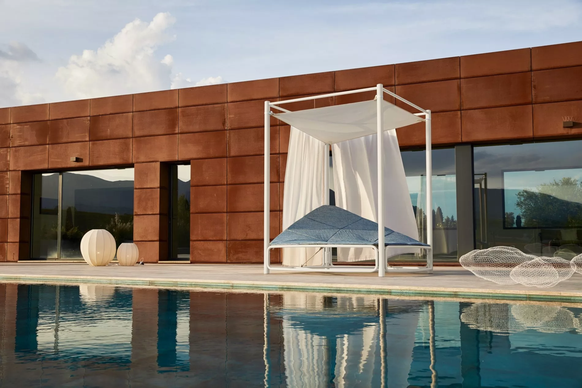 Atollo Daybed von Roberti in Weiß und Blau, 200x200 cm, auf einer modernen Terrasse mit Pool und Bergblick im Hintergrund.