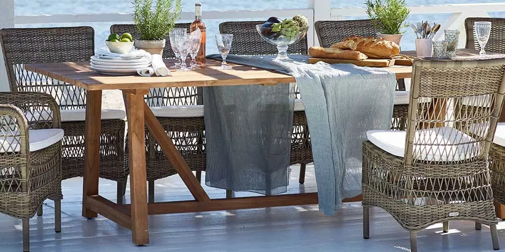 Sika-Design George Essgruppe aus braunem Rattan und Holz auf einer Terrasse mit gedecktem Tisch und Meerblick im Hintergrund.