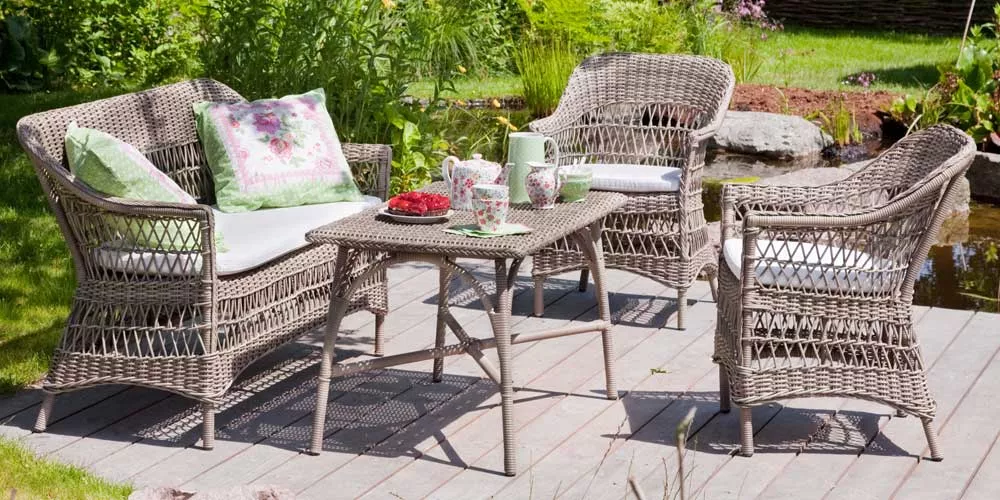 Sika Design Victoria Essgruppe aus Rattan in Naturfarbe auf Holzterrasse im Garten, bestehend aus Sofa, zwei Sesseln und Tisch.