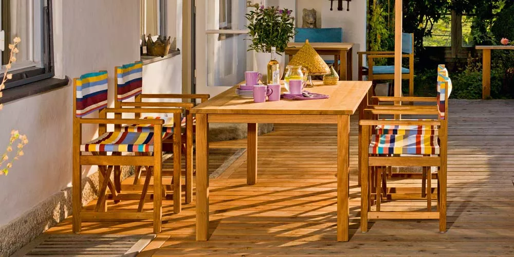 Weißhäupl Cabin Gartenmöbel-Set aus Holz mit bunten Streifenpolstern auf einer Terrasse bei Sonnenschein.