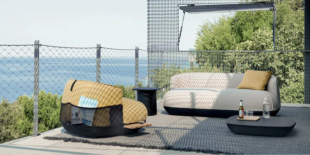 Kristalia Brioni Outdoor-Sofa in Beige und Grau auf einer Terrasse mit Meerblick und modernem Hintergrund.