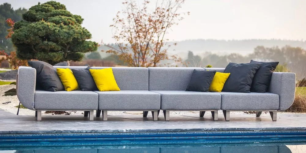 Grau-gelbe Todus Lotus Outdoor-Sofa-Kollektion auf einer Terrasse mit Pool und Naturhintergrund.