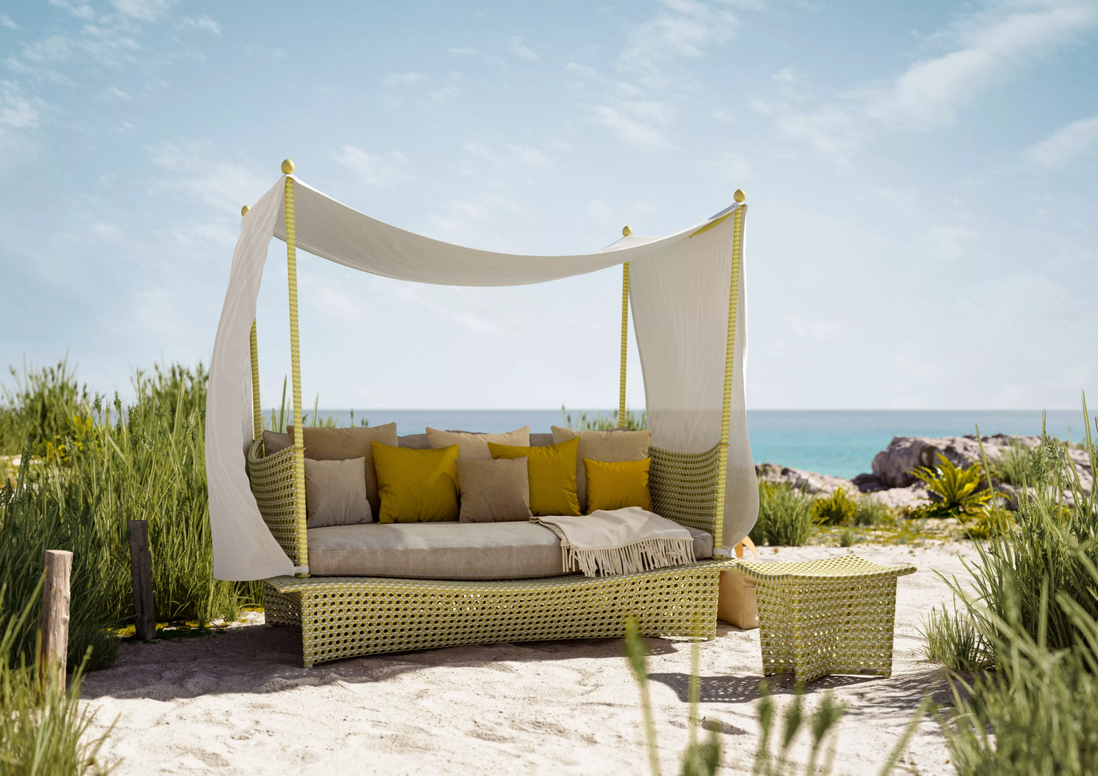 DEDON DAYDREAM Loungeinsel mit Kissen und Decke steht am Strand unter blauem Himmel und lädt zum Entspannen ein