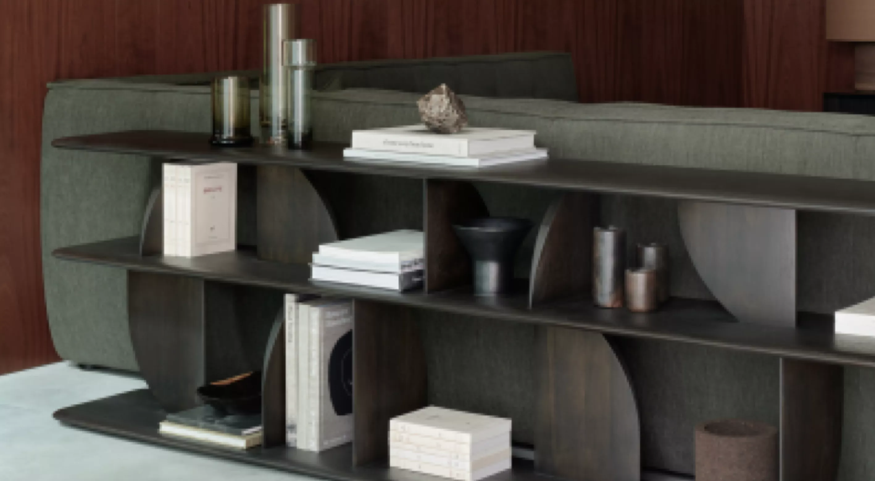 Braune Muuto Compile Regalwand vor grünem Sofa, dekoriert mit Büchern und Vasen, in modernem Wohnzimmer mit Holzwand im Hintergrund.