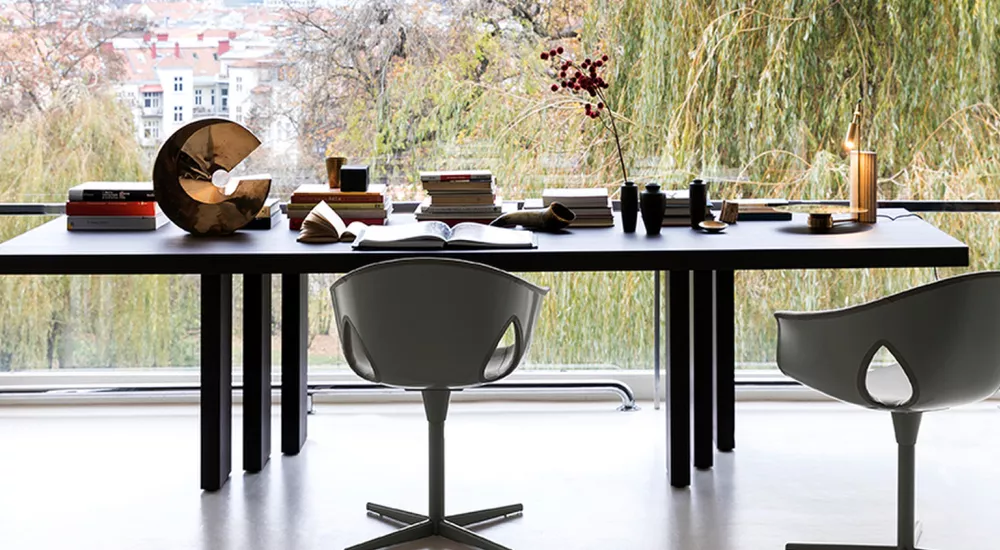 Poltrona Frau Ginger Ale Stühle in Grau vor einem großen Fenster mit Blick auf eine herbstliche Landschaft, moderne Büroeinrichtung.
