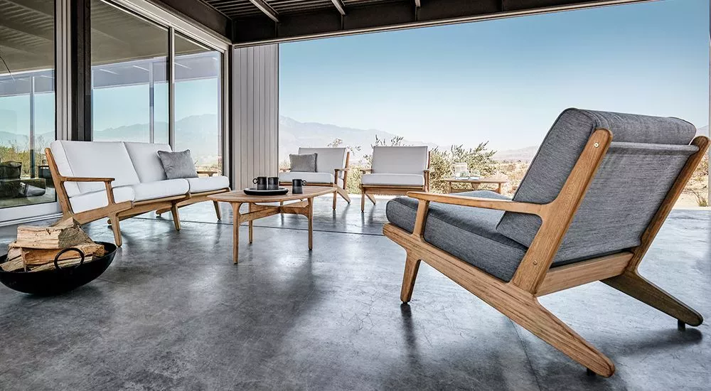Gloster Bay Lounge in Grau und Naturholz auf einer Terrasse mit Bergblick, moderne Outdoor-Möbel in entspannter Atmosphäre.