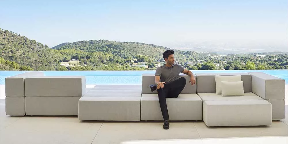 Ein Mann sitzt auf der grauen Vondom Tablet Loungegruppe vor einem Pool mit Bergblick im Hintergrund.