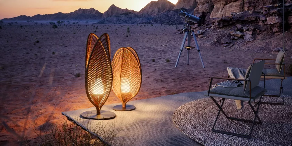 Zwei DEDON Scoora Leuchten in warmem Orange auf einer Terrasse in der Wüste bei Sonnenuntergang, neben einem Teleskop und Stühlen.