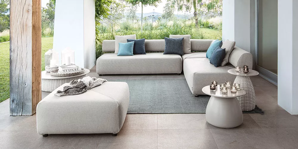 Dedon Kollektion Brixx zeigt eine moderne Outdoor-Sitzgruppe mit hellen Polstern und Kissen in einem offenen Raum mit Blick auf die Natur