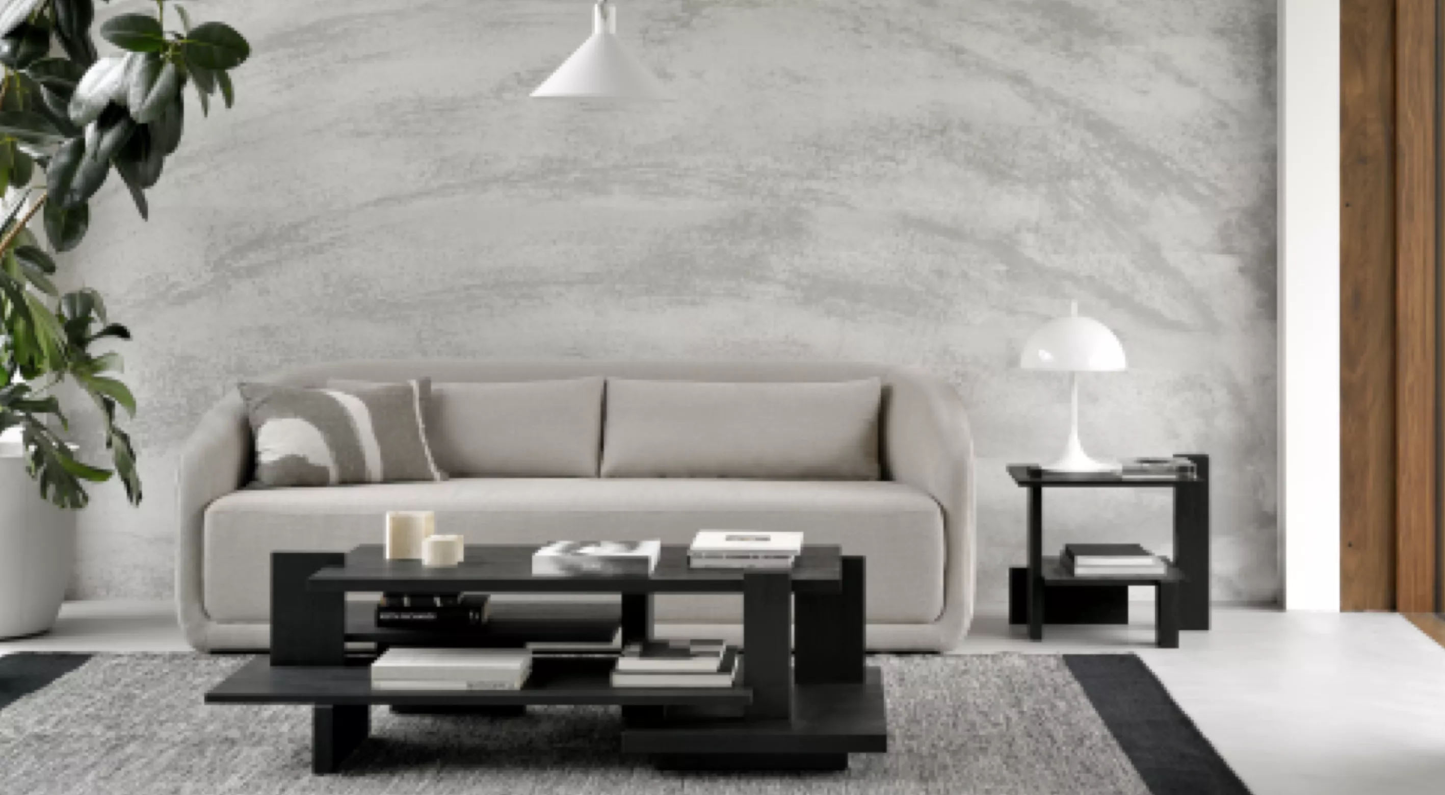 Graues Sofa und schwarzer Couchtisch von Villa Schmidt in modernem Wohnzimmer mit Betonwand und Pflanzen im Hintergrund.