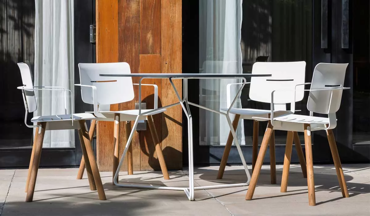 Oasiq Coco Gartenmöbel-Set in Weiß mit Holzelementen, bestehend aus einem Tisch und vier Stühlen, auf einer Terrasse vor einem Holzhaus.