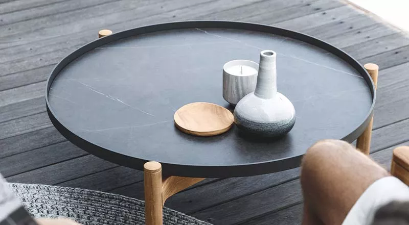 Gloster Sepal Couchtisch in Schwarz auf Holzterrasse, mit Kerze und Vase dekoriert, stimmungsvolles Bild aus der Vogelperspektive.