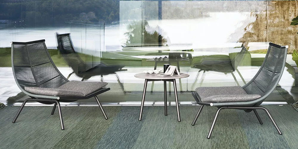 Zwei graue Roda Laze Loungesessel und ein runder Tisch auf einer Terrasse mit Seeblick, moderne und entspannte Atmosphäre.