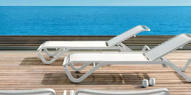 Zwei weiße Ethimo Ocean Outdoor-Sonnenliegen auf einer Holzterrasse mit Blick auf das blaue Meer bei klarem Himmel.