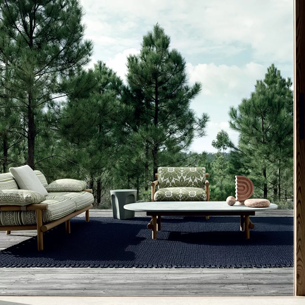 B&B Italia Ayana Loungesessel und Sessel auf einer Terrasse mit Wald im Hintergrund und einem Tisch mit Dekorationen