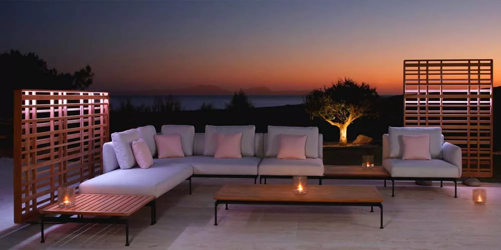 Barlow Tyrie Layout Loungegruppe in Weiß auf Terrasse bei Sonnenuntergang, mit Holztischen und Kerzen, stimmungsvolle Abendatmosphäre.