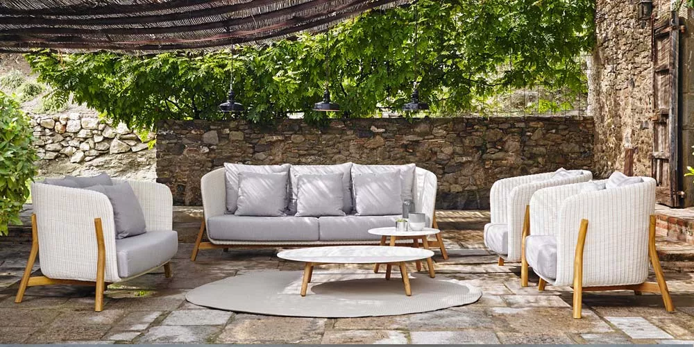 Outdoor-Loungegruppe von Point, Modell Round, in Weiß und Grau, auf einer Terrasse mit Steinboden und grüner Pflanzenkulisse.