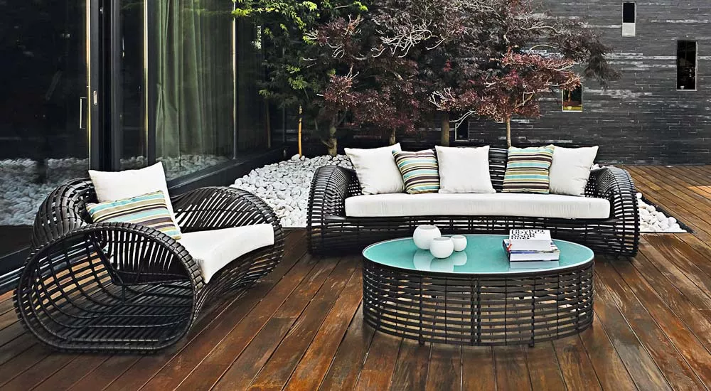 Kenneth Cobonpue Lolah Loungegruppe in Schwarz auf Holzterrasse vor modernem Gebäude, bestehend aus Sofa, Sessel und Tisch mit Glasplatte.
