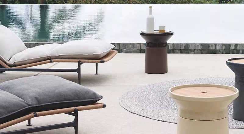 Gemütliche Outdoor-Szene mit Gloster Coso Beistelltisch in Braun neben einer Liege am Pool auf einer Terrasse.