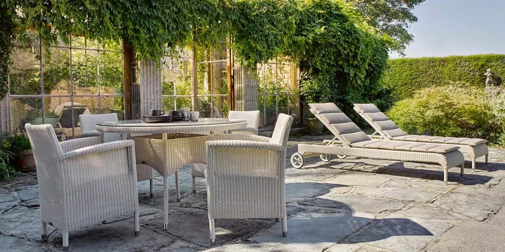 Vincent Sheppard Safi Gartenmöbel-Set in Beige auf einer sonnigen Terrasse mit grüner Pflanzenkulisse und Steinboden.