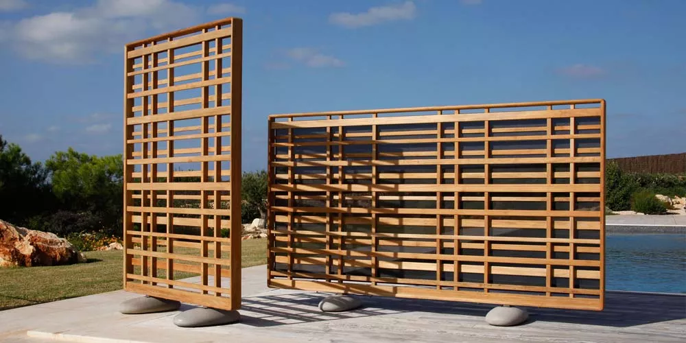 Barlow Tyrie Woodland Trennwände aus Holz in natürlichem Braun, freistehend auf einer Terrasse mit Blick auf einen sonnigen Garten.