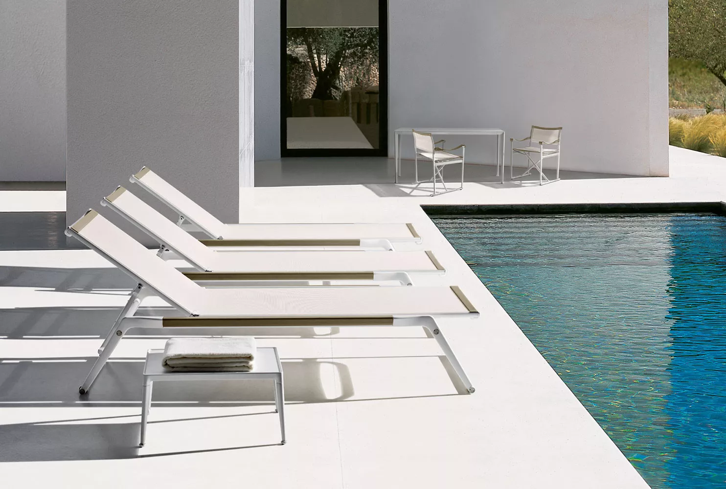 Drei B&B Italia Mirto Outdoor Liegestühle stehen nebeneinander am Pool im Freien im Hintergrund sind ein Tisch und zwei Stühle zu sehen