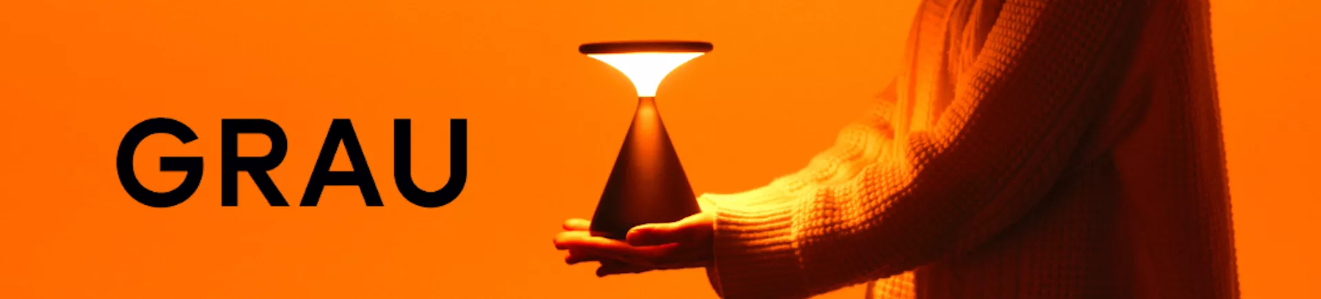 Person hält eine schwarze GRAU Tischlampe vor orangefarbenem Hintergrund, stimmungsvolles Bild.